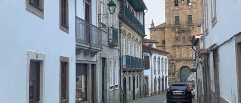 Een smalle straat met kinderaardewerk, begrensd door historische gebouwen met balkons en een opvallende toren op de achtergrond.