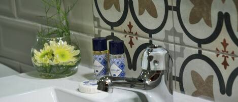 A bathroom sink with a faucet, a glass vase with flowers, and two toiletry bottles.