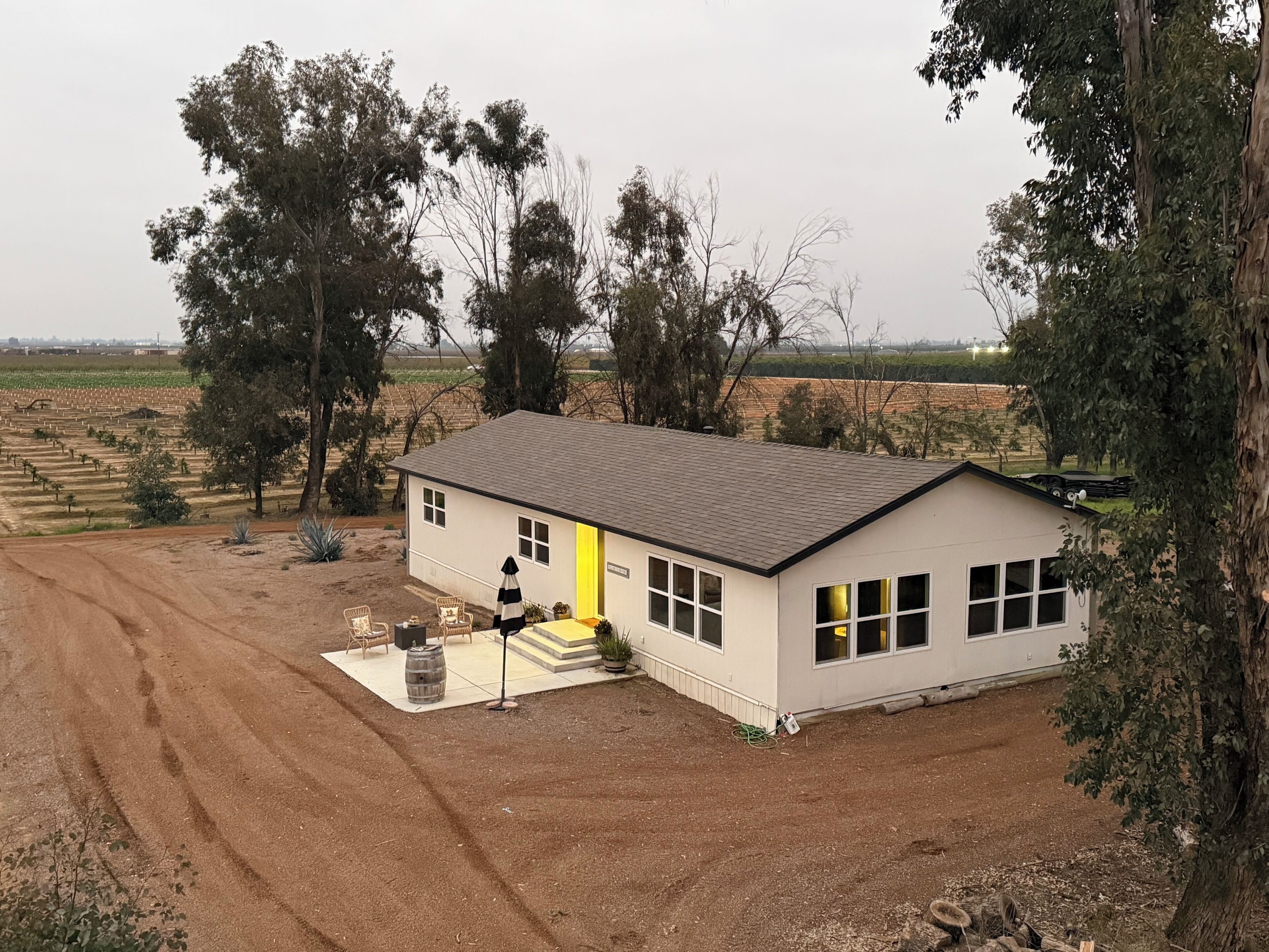 Une maison de plain-pied avec une porte jaune, entourée d’arbres et donnant sur une allée non pavée.