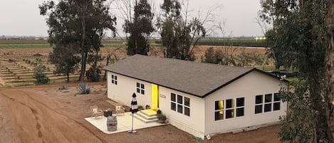 Ein eingeschossiges Haus mit gelber Tür, umgeben von Bäumen und einer unbefestigten Einfahrt.
