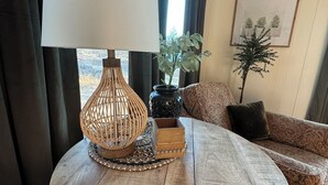 Una mesa de centro redonda de madera con una lámpara trenzada, una planta en maceta y un cuadro en la pared.