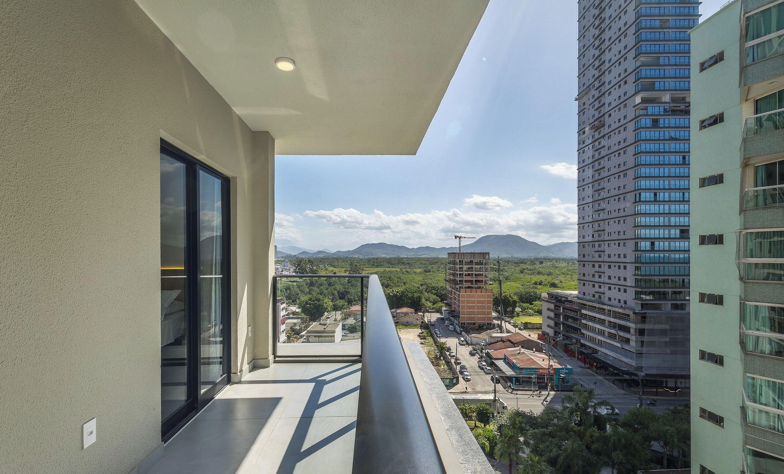 A balcony with a view of a cityscape, including a building under construction and mountains in the distance.