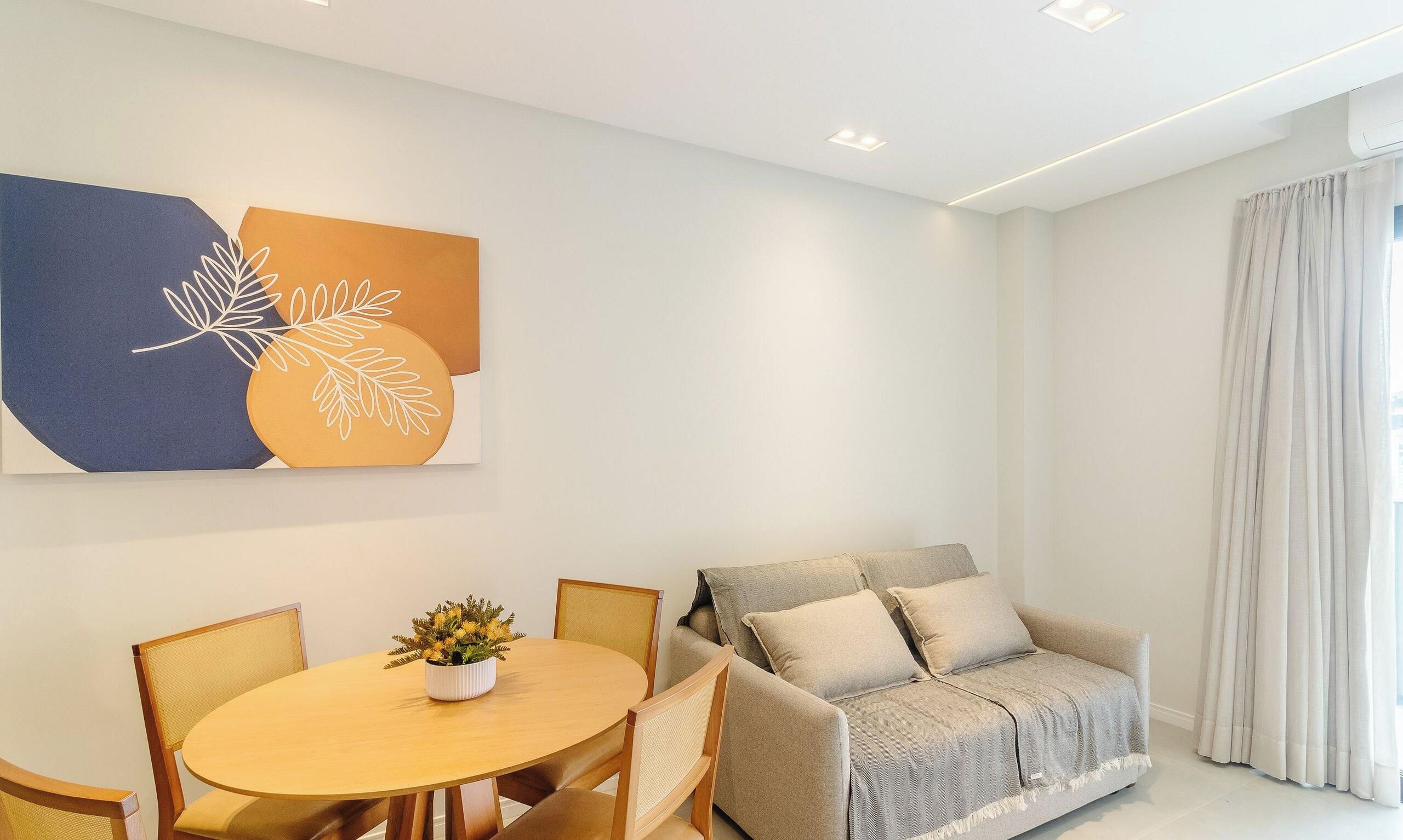 A modern living room with a round wooden table, two chairs, a sofa with cushions, and a wall-mounted abstract art piece.