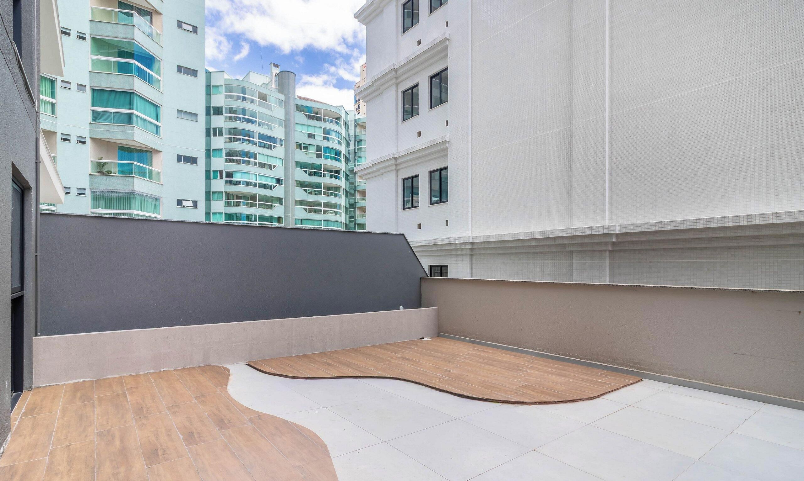 Terraço no telhado com deck de madeira e parede cinza.