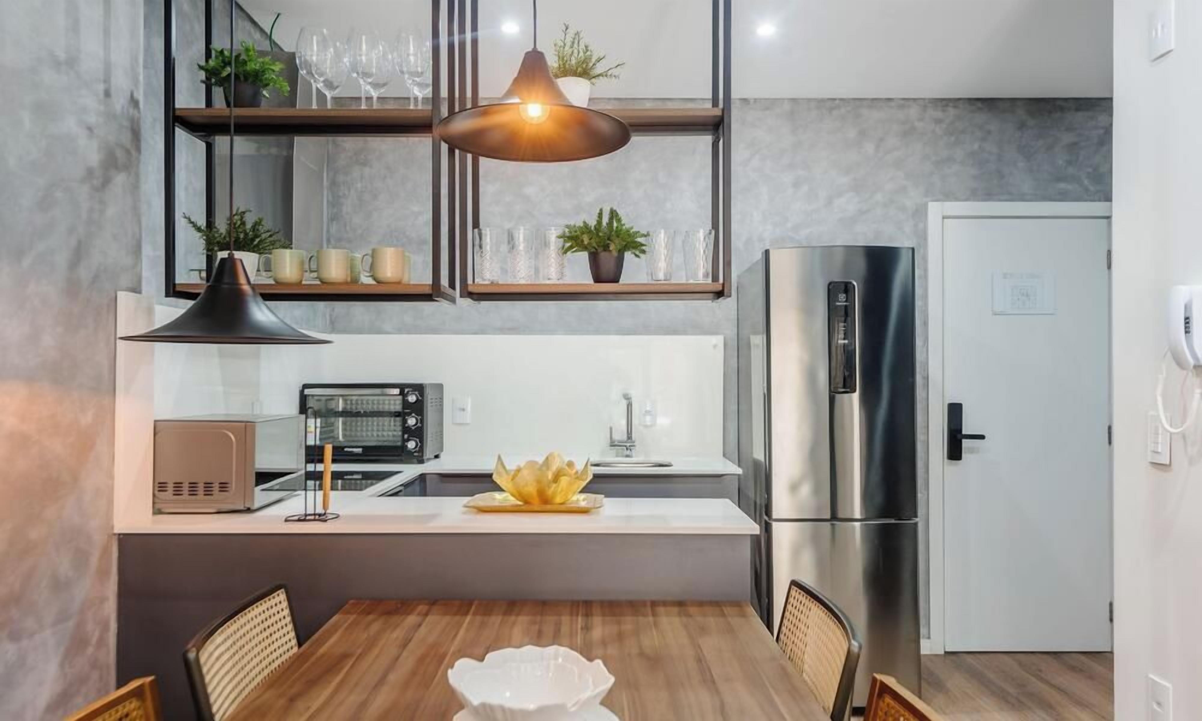 Eine moderne Küche mit integriertem Kühlschrank, Mikrowelle und Kaffeemaschine. Ein Esstisch mit Stühlen und einer Pendelleuchte darüber.