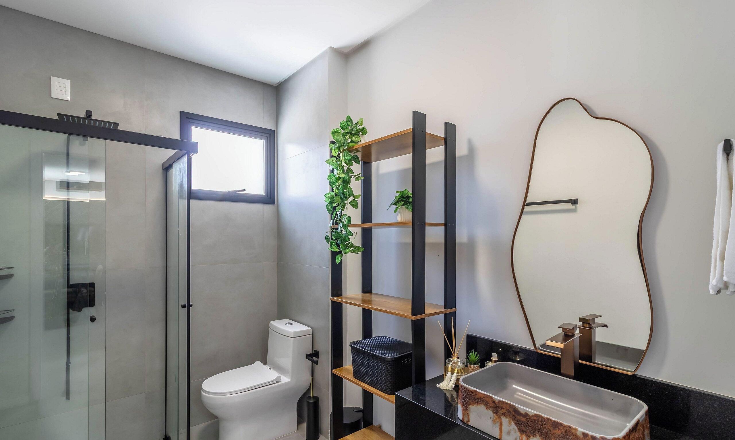 A modern bathroom with a glass shower enclosure, a toilet, a black sink, and a wooden shelf with a plant.
