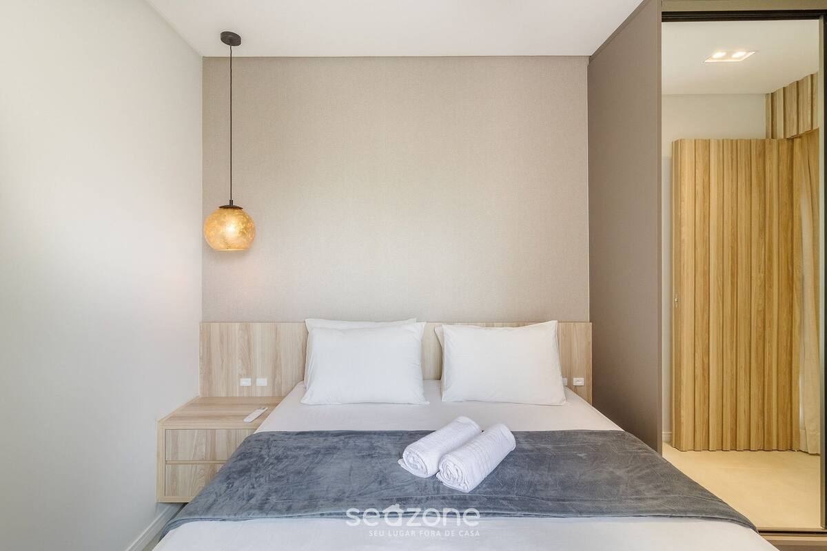 A modern hotel room with a bed, a bedside table, a wall-mounted light, and a curtain.