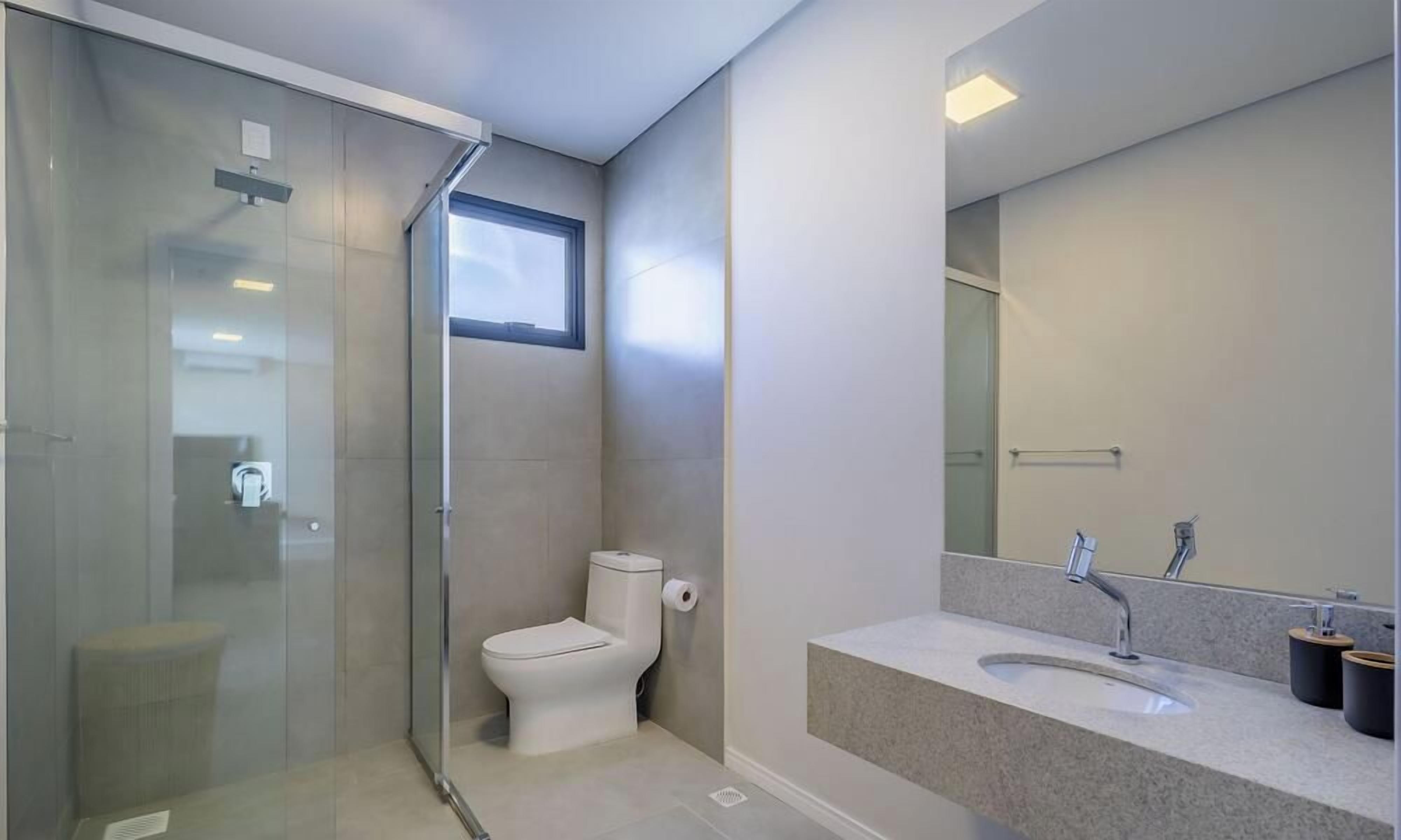 A modern bathroom with a glass shower enclosure, a toilet, and a sink with a mirror.