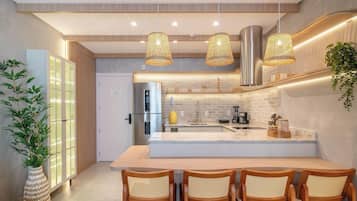 Cozinha moderna com ilha central, eletrodomésticos de aço inoxidável e área de estar com cadeiras de madeira.