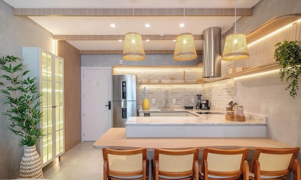 A modern kitchen with a central island, stainless steel appliances, and a seating area with wooden chairs. - Sua estadia exclusiva a poucos passos do Mar em Meia Praia - FFS (Itapema)