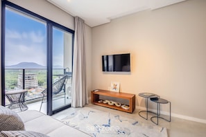 A modern living room with a large sliding glass door leading to a balcony, a flat-screen TV mounted on the wall, a wooden console table, and a patterned rug. - Sua estadia exclusiva a poucos passos do Mar em Meia Praia - FFS (Itapema)