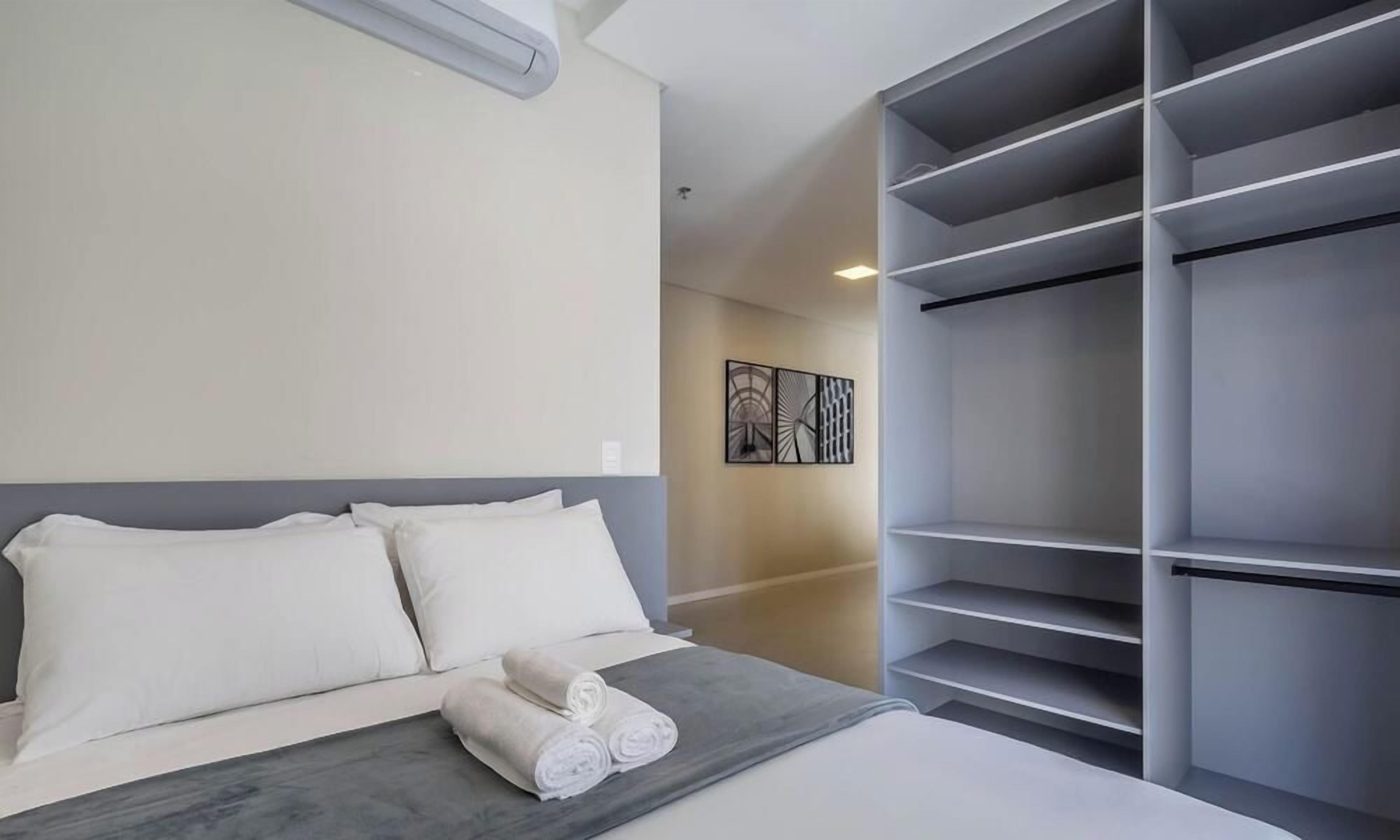 A hotel room with a bed, a grey headboard, a wall-mounted air conditioner, and a large grey wardrobe.
