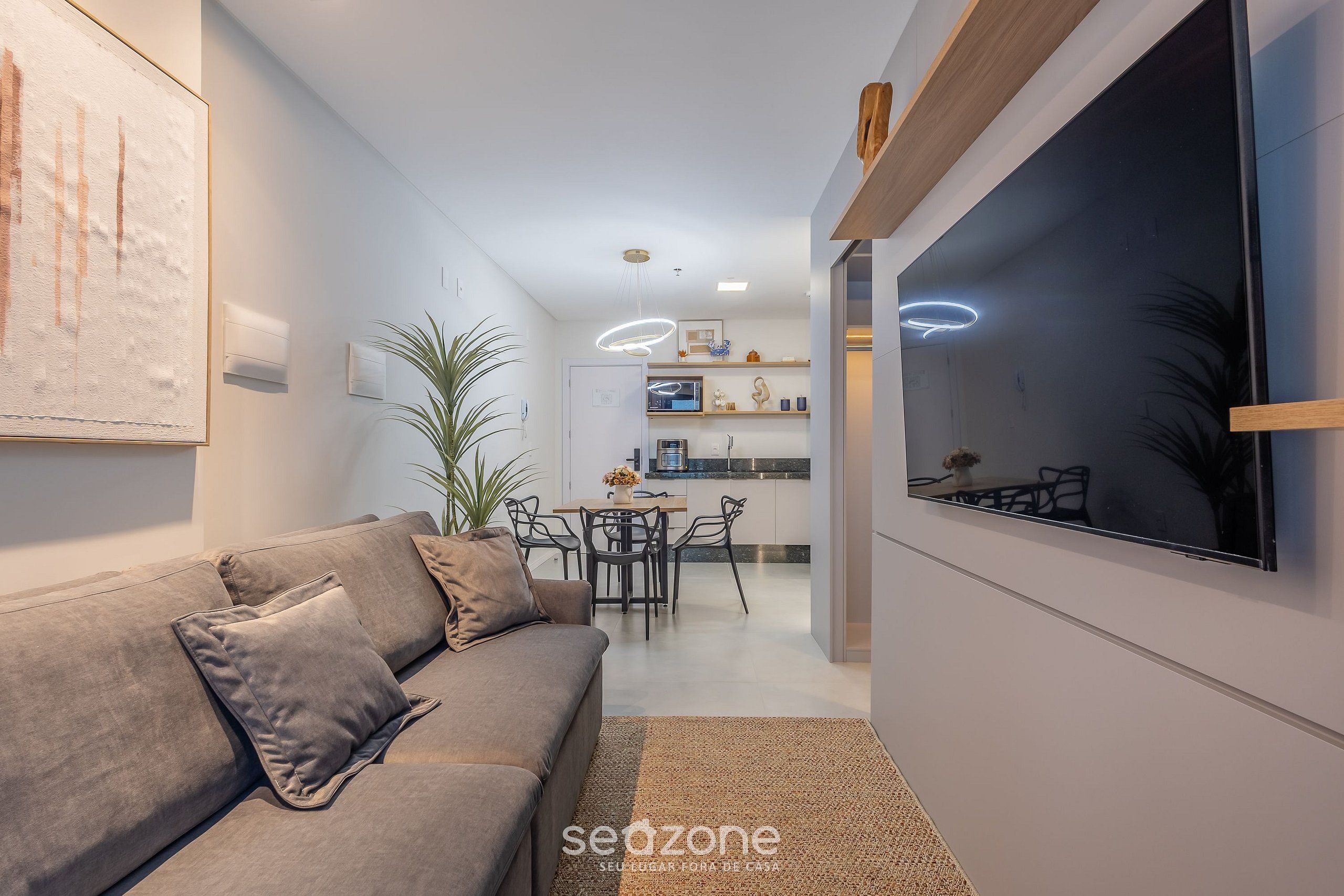 Ein modernes Wohnzimmer mit einer Couch, einem Fernseher und einer Küche im Hintergrund.