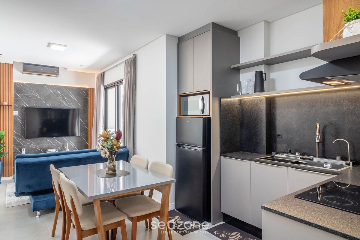 A modern kitchen with a built-in oven, a refrigerator, and a sink. There is a dining area with a table and chairs.