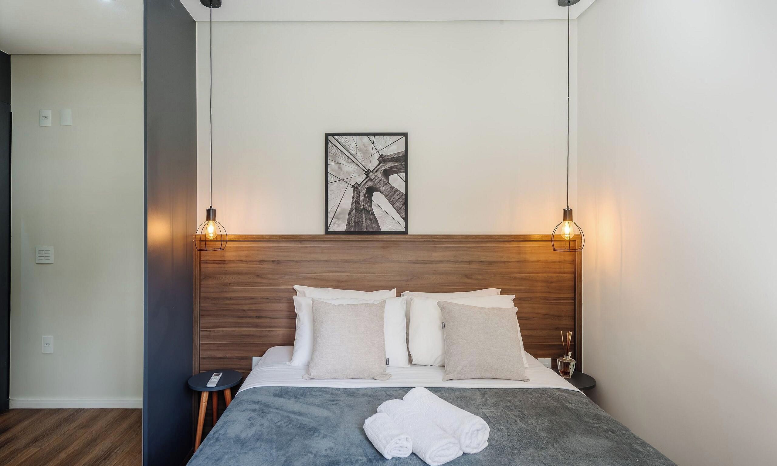 A hotel room with a wooden headboard, a bed with white bedding, two bedside tables, and a framed picture on the wall.