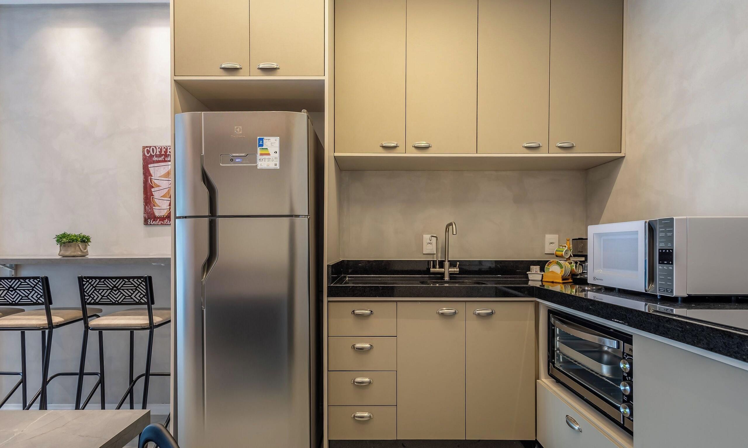 Une cuisine moderne équipée d’appareils électroménagers en acier inoxydable, notamment un réfrigérateur, un four à micro-ondes et un four traditionnel. On y trouve des armoires de couleur beige, un plan de travail noir et un petit coin repas avec deux chaises.