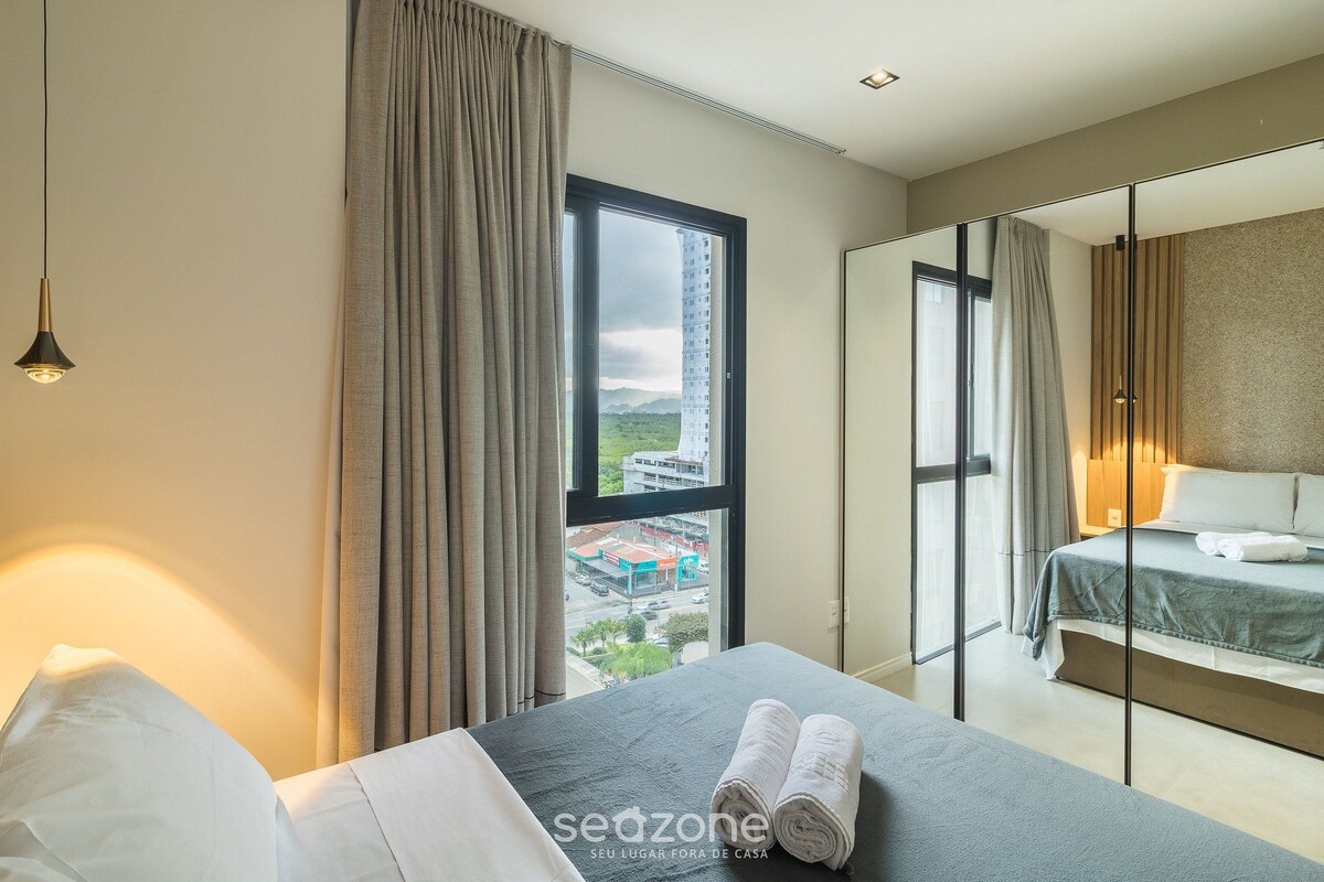 A hotel room with a bed, a view of the city, and a large window.