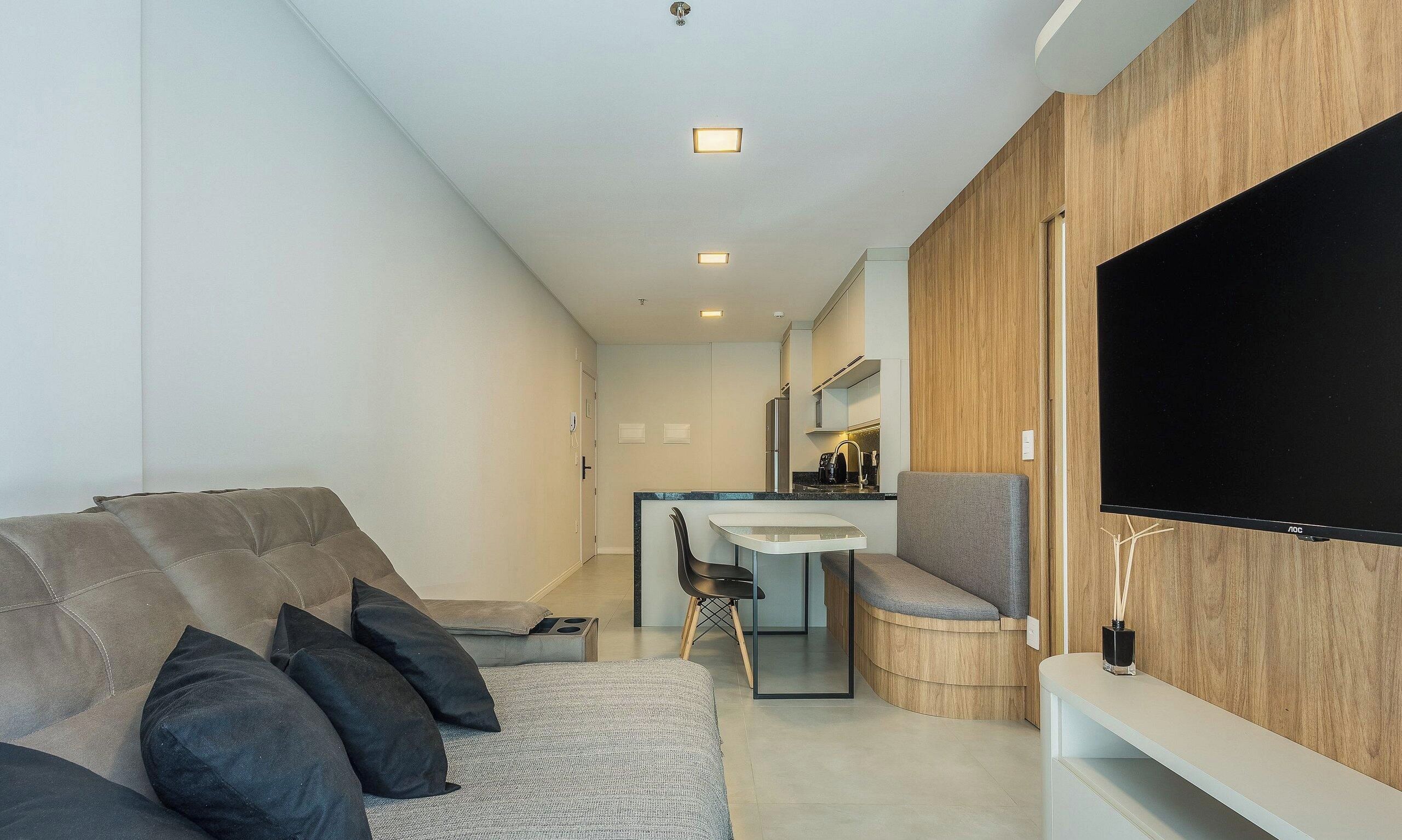 A modern living room with a sofa, a dining table, and a TV mounted on the wall.