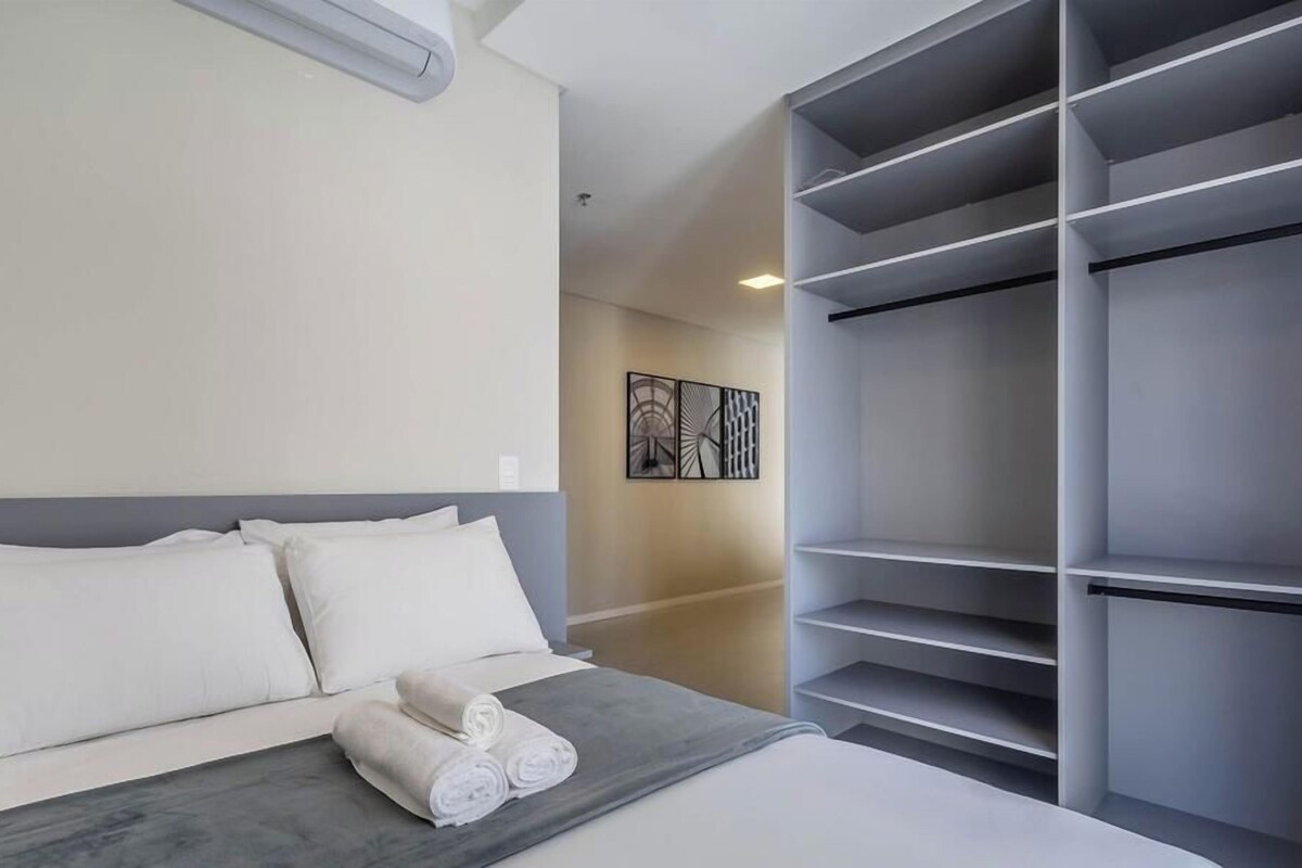 A hotel room with a bed, a grey headboard, a large wardrobe, and a wall-mounted artwork.
