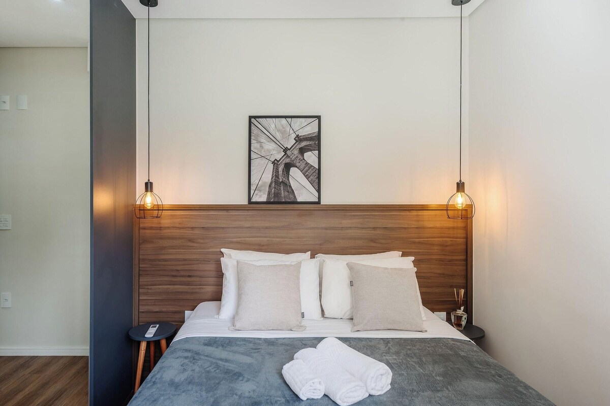 A hotel room with a wooden headboard, a bed with white bedding, two bedside tables, and a framed picture on the wall.