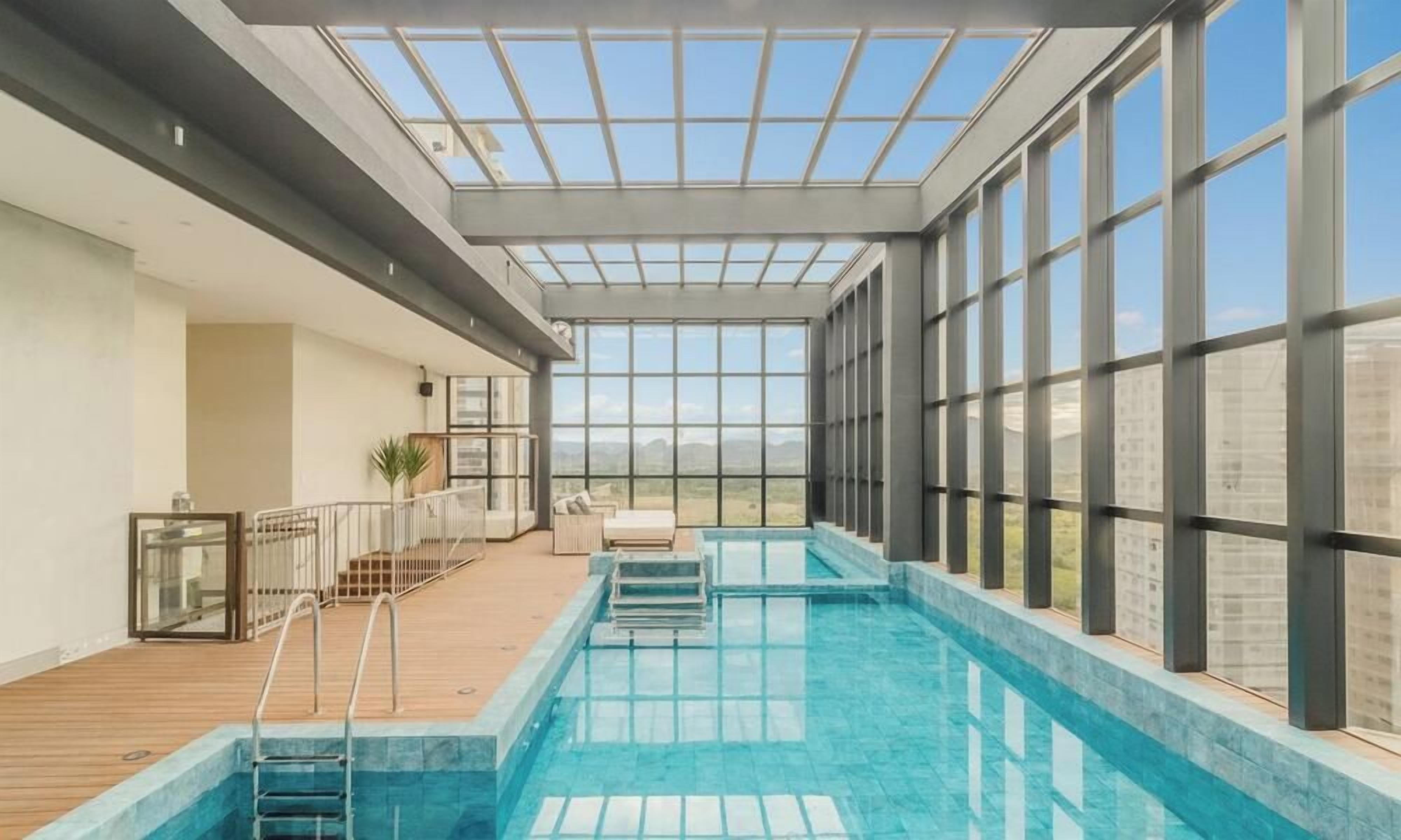 A swimming pool with a glass ceiling, wooden deck, and a view of the mountains.