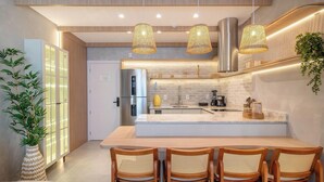A modern kitchen with a central island, stainless steel appliances, and hanging wicker light fixtures. - Sua estadia exclusiva a poucos passos do Mar em Meia Praia - FFS (Itapema)