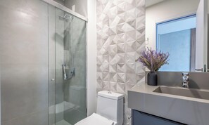 A modern bathroom with a glass-enclosed shower, a toilet, and a sink with a mirror above it. - Sua estadia exclusiva a poucos passos do Mar em Meia Praia - FFS (Itapema)