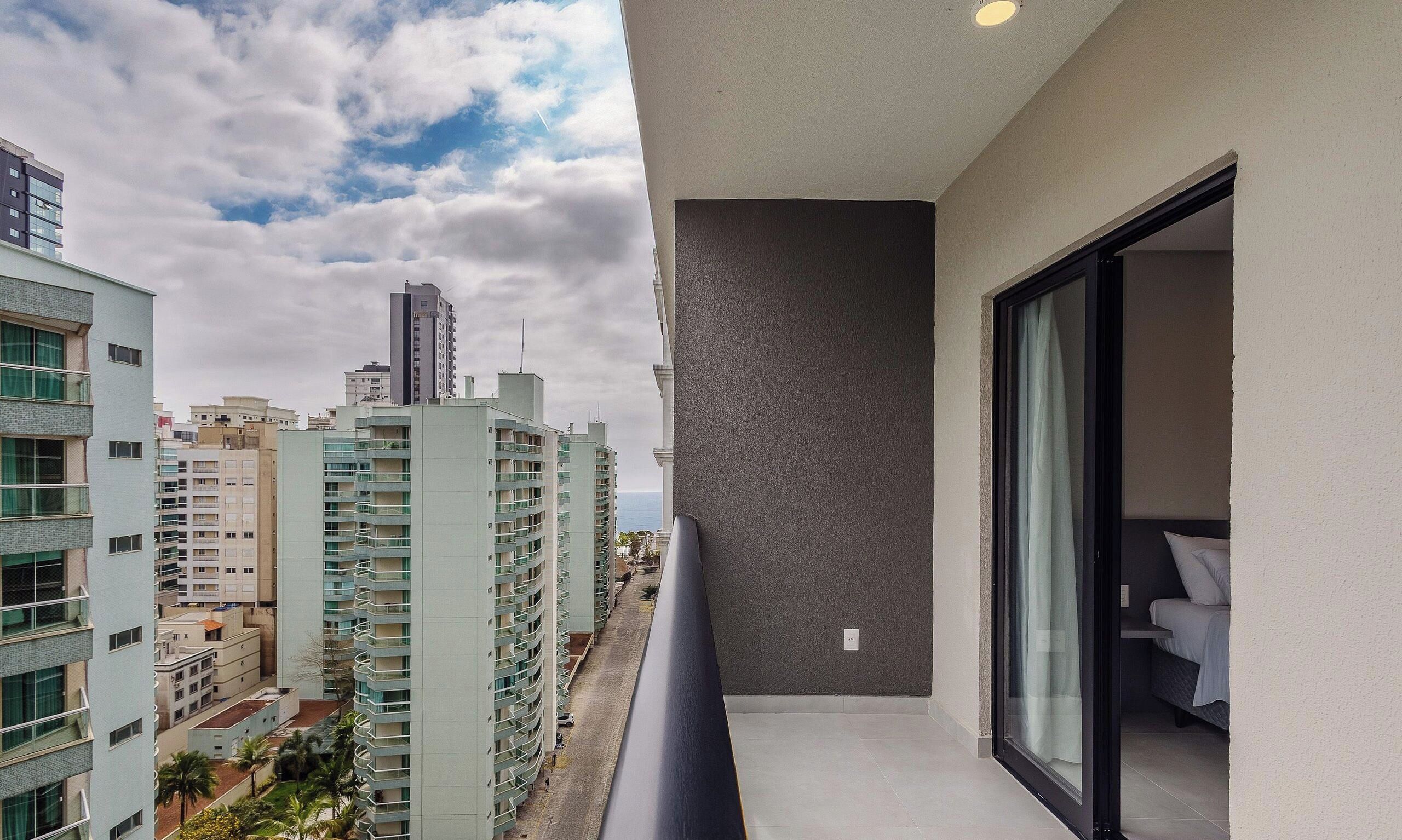 A balcony with a view of a cityscape and a building with a grey wall and a window.
