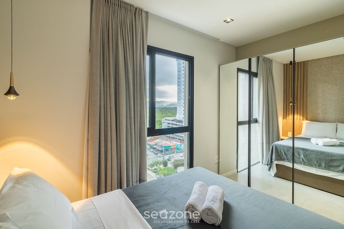 A hotel room with a bed, a view of the city, and a large window.