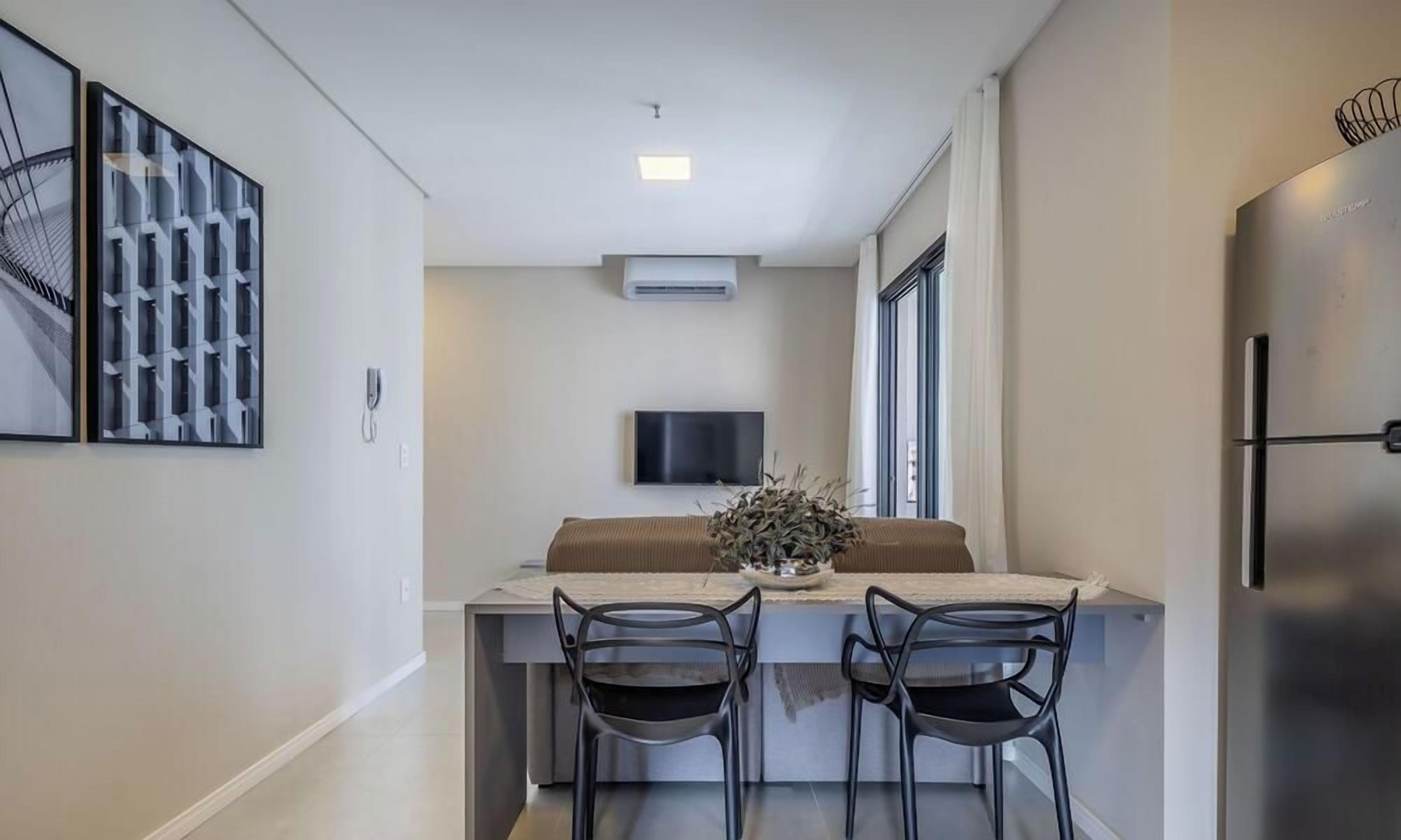 Una cocina moderna con refrigerador integrado, un televisor de pantalla plana montado en la pared y un comedor con dos sillas y una mesa.