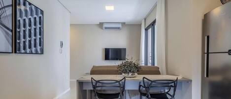 A modern kitchen with a built-in refrigerator, a flat-screen TV mounted on the wall, and a dining area with two chairs and a table.