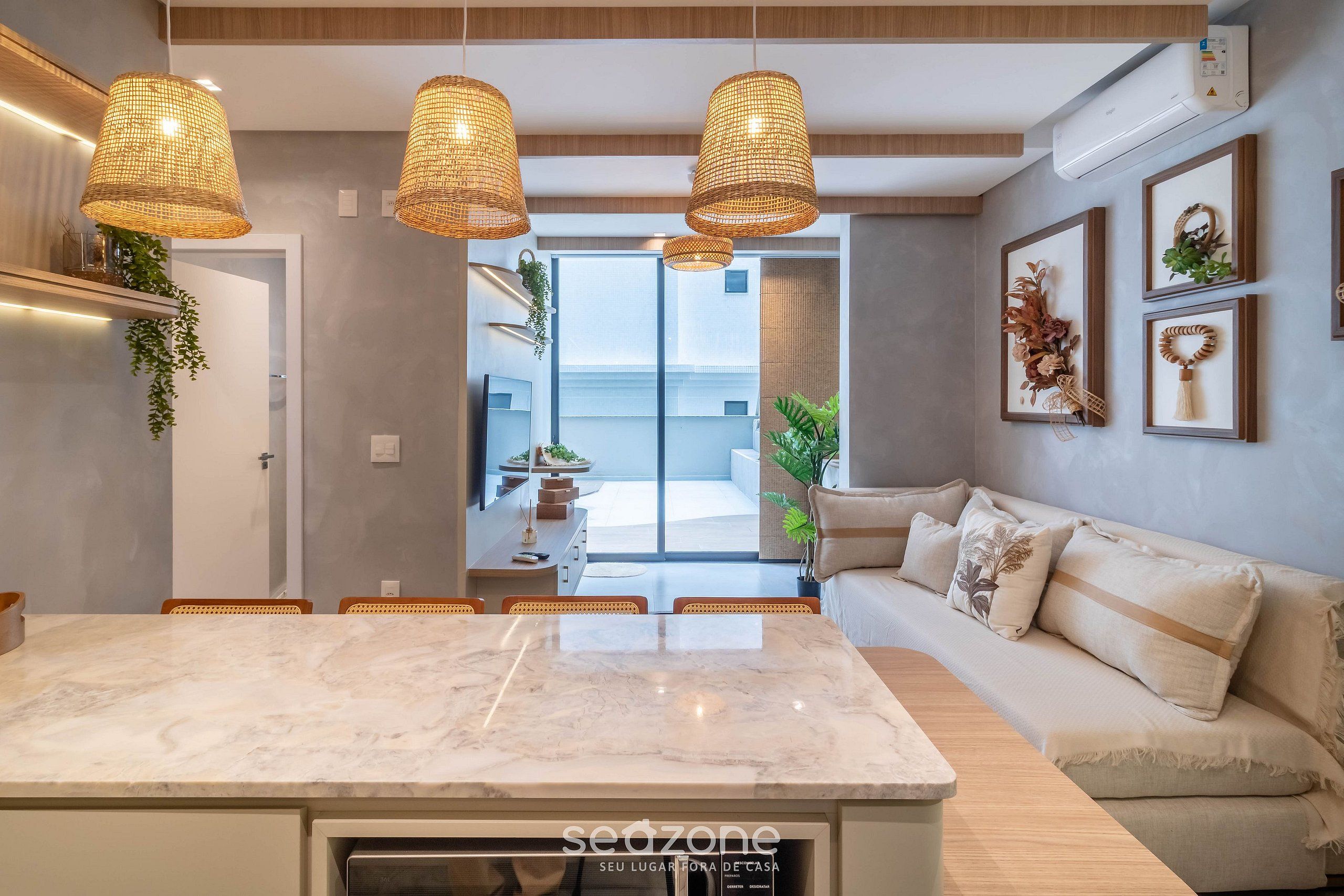 A modern kitchen with a marble countertop, wicker pendant lights, a built-in oven, and a view to the outside.