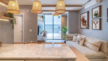 A modern kitchen with a marble countertop, wicker pendant lights, a built-in oven, and a view to the outside.
