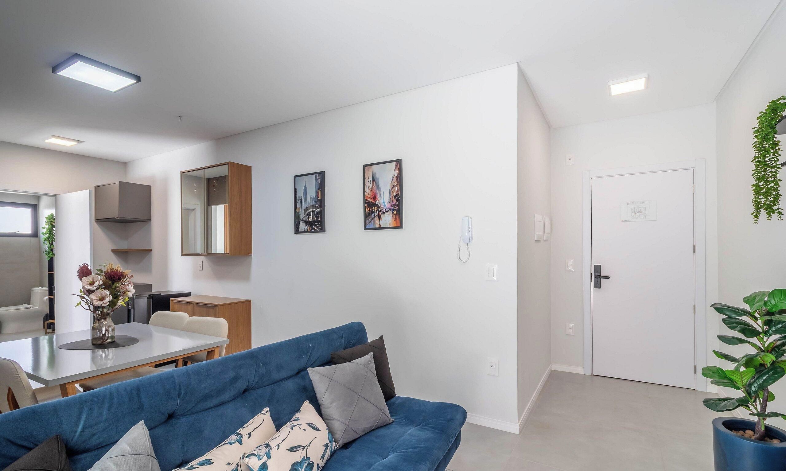 A modern living room with a blue sofa, a dining table, and a kitchen area with cabinets and a refrigerator.