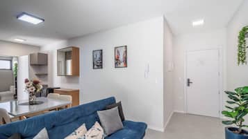 Una sala de estar moderna con un sofá azul, una mesa de comedor y una zona de cocina con armarios y un refrigerador.