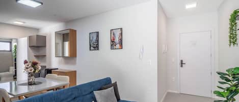 A modern living room with a blue sofa, a dining table, and a kitchen area with cabinets and a refrigerator.