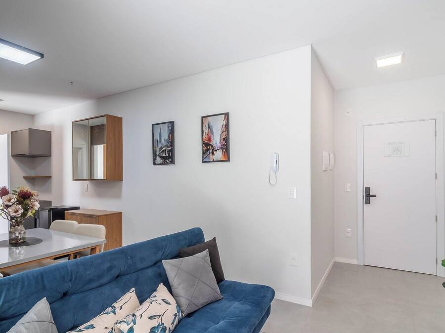 A modern living room with a blue sofa, a dining table, and a kitchen area with cabinets and a refrigerator.