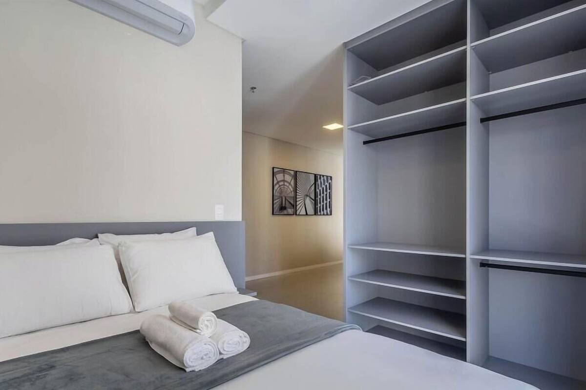 A hotel room with a bed, a gray headboard, a large wardrobe, and a wall-mounted artwork.