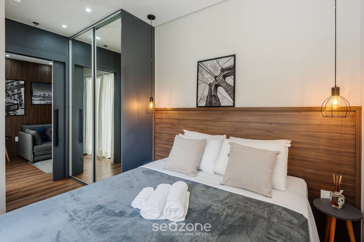 A modern hotel room with a large bed, a mirror, a framed picture, and a small table with a candle.