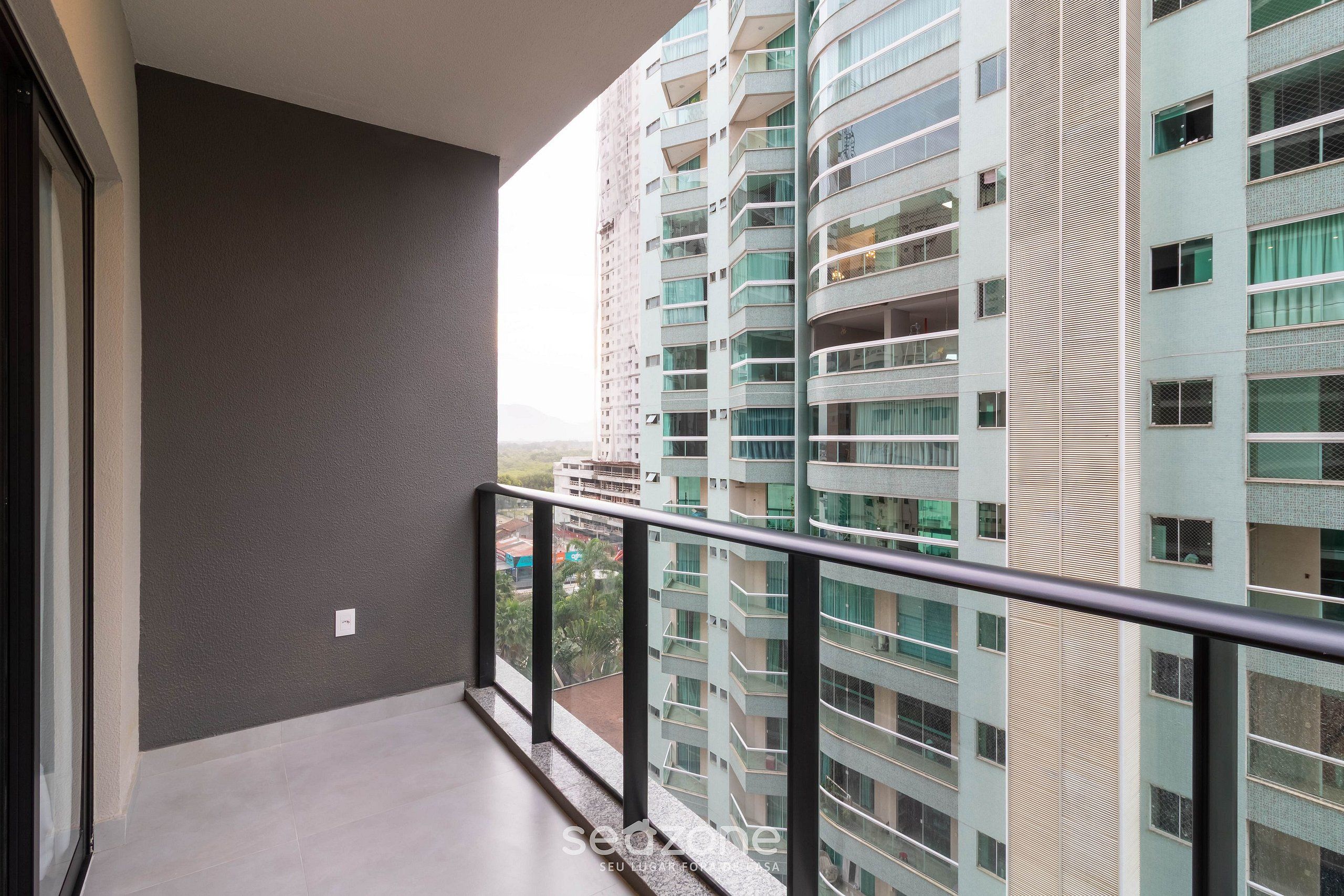 Uma varanda com grade de metal, com vista para um edifício alto com várias varandas e janelas.