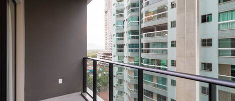 Uma varanda com grade de metal, com vista para um edifício alto com várias varandas e janelas.