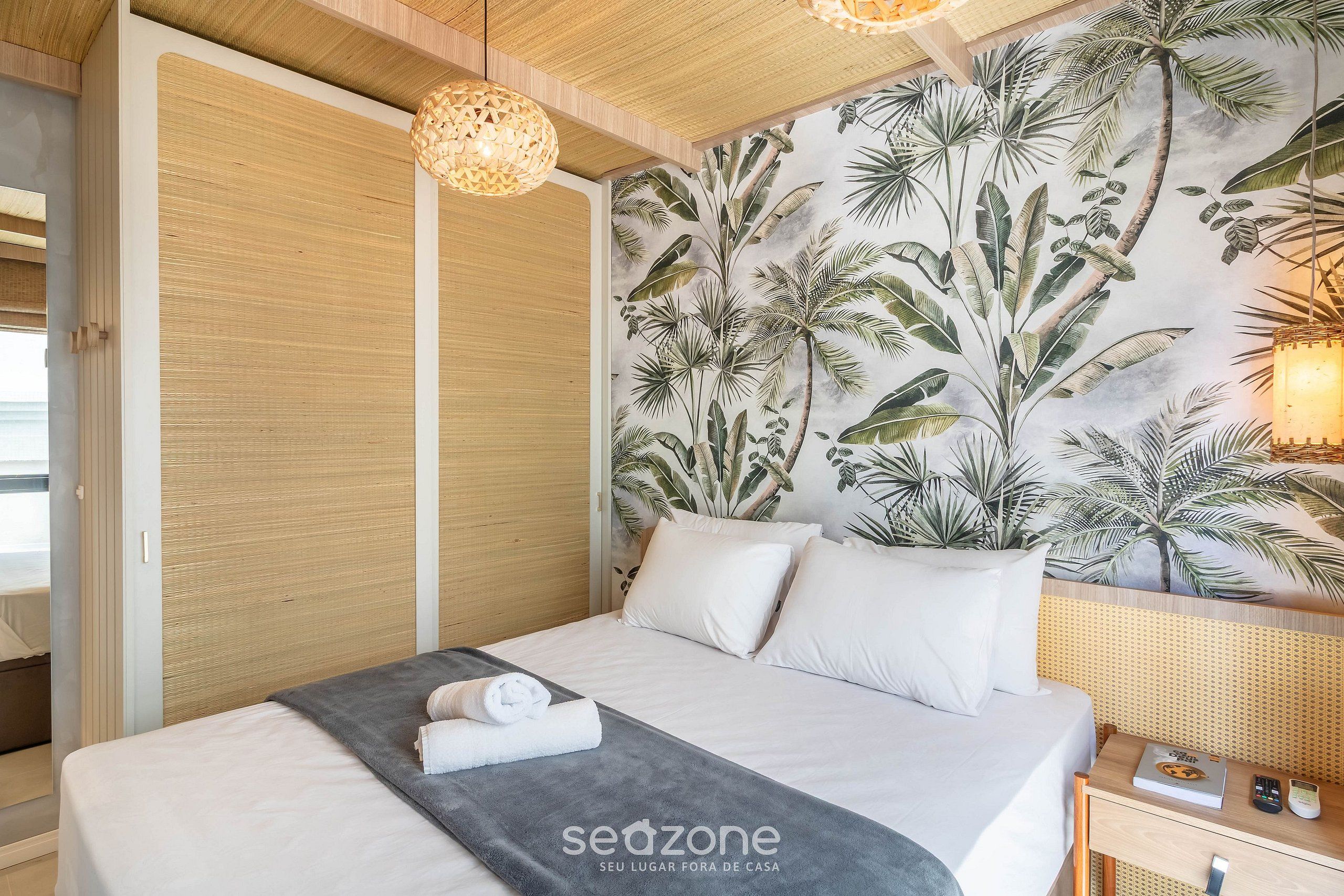 A hotel room with a bed, a bedside table with a lamp, a wall with a tropical mural, and a wardrobe.