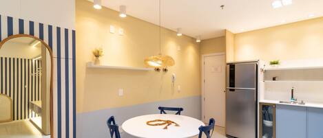 A modern kitchen with a round dining table, chairs, a refrigerator, and a hanging light fixture.