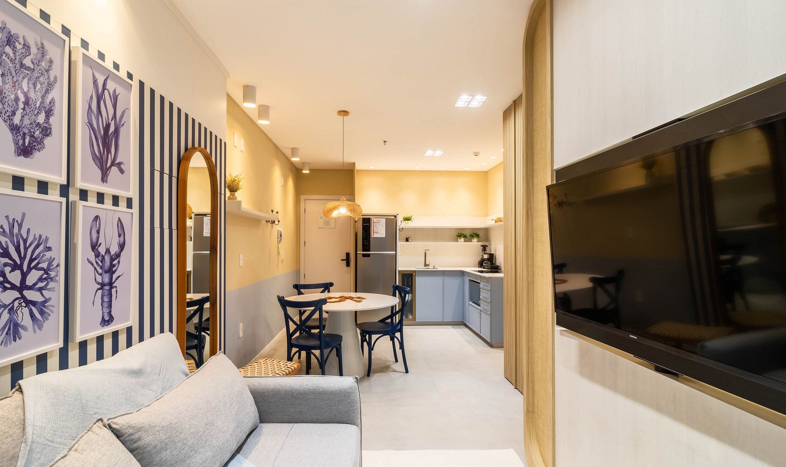 A modern interior with a sofa, dining table, chairs, kitchen area, and a large TV screen.