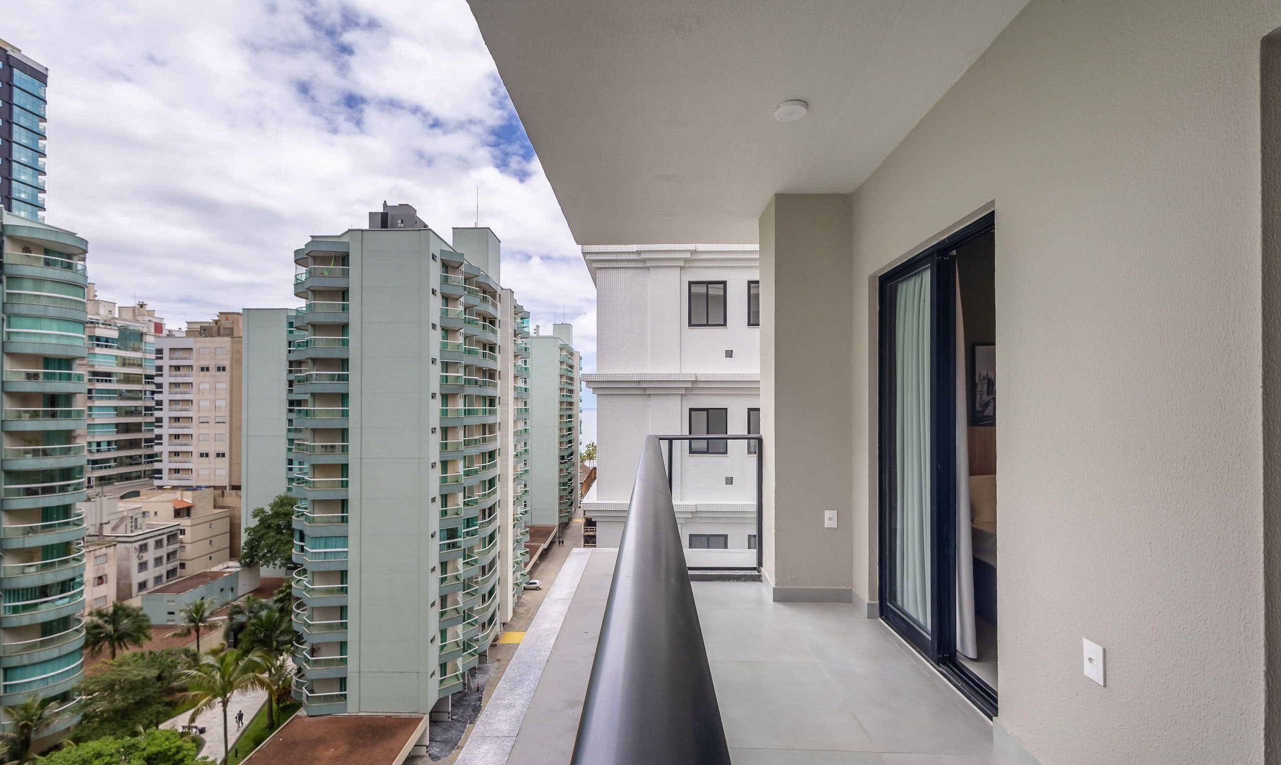 A balcony with a view of high-rise buildings, a clear sky, and a door leading to the interior.