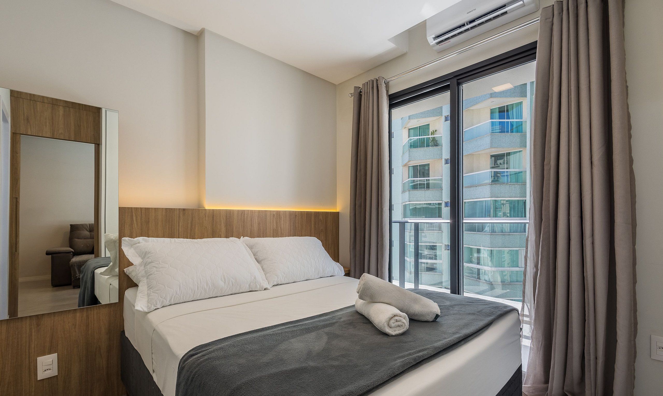 Una camera d'albergo con un letto, uno specchio, un condizionatore d'aria e una finestra con tende.