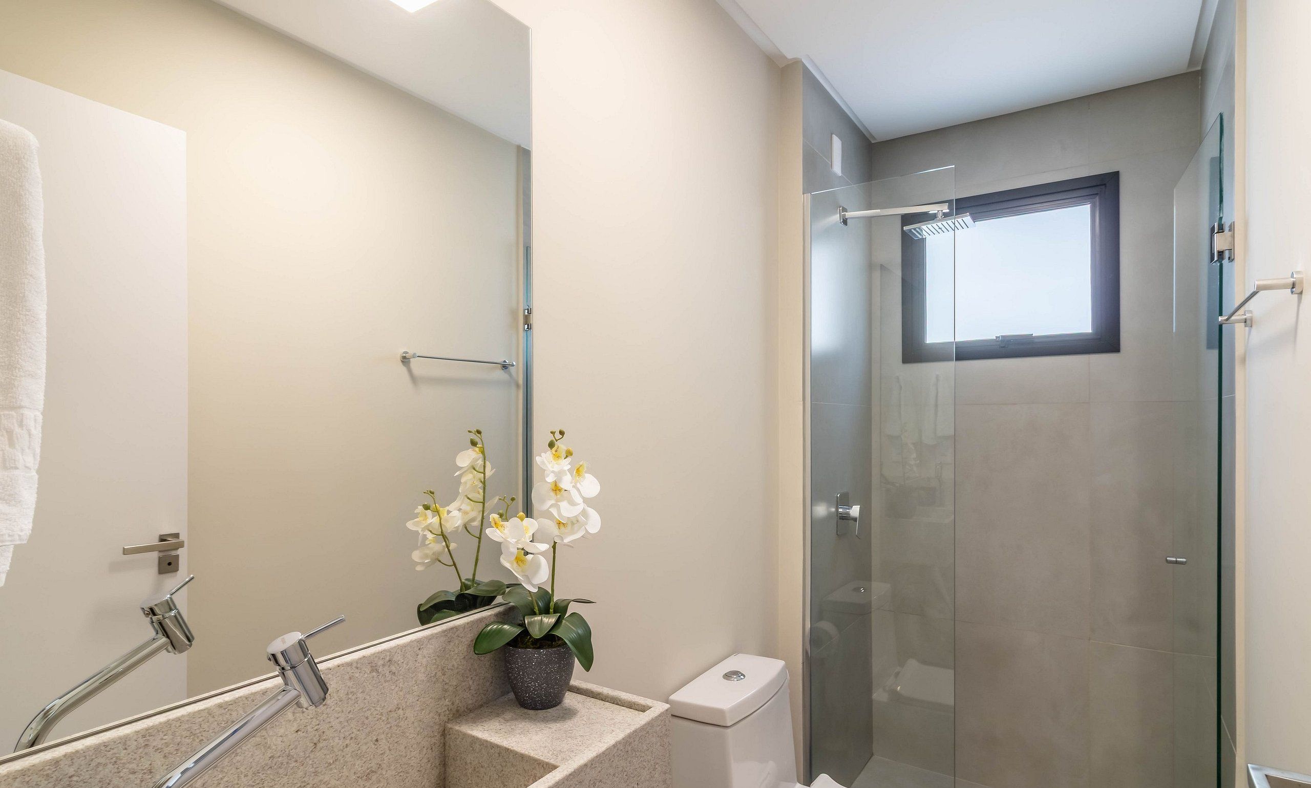 Un baño moderno con cabina de ducha de vidrio, un lavabo con espejo y una orquídea en maceta.
