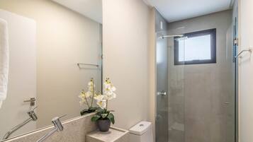 Un baño moderno con cabina de ducha de vidrio, un lavabo con espejo y una orquídea en maceta.