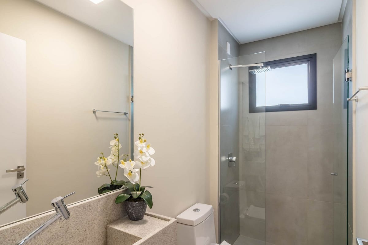 A modern bathroom with a glass shower enclosure, a sink with a mirror, and a potted orchid.