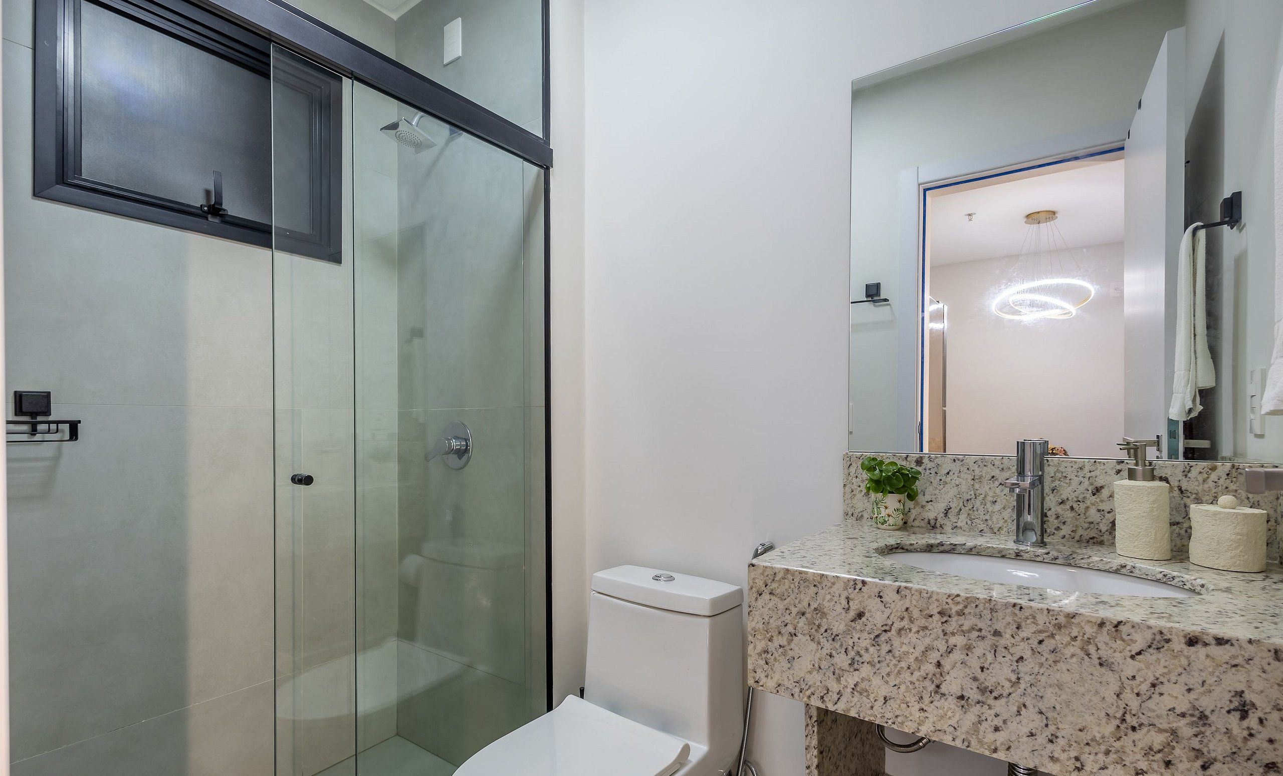 Uma casa de banho moderna com chuveiro de vidro, sanita branca e lavatório com bancada de granito.